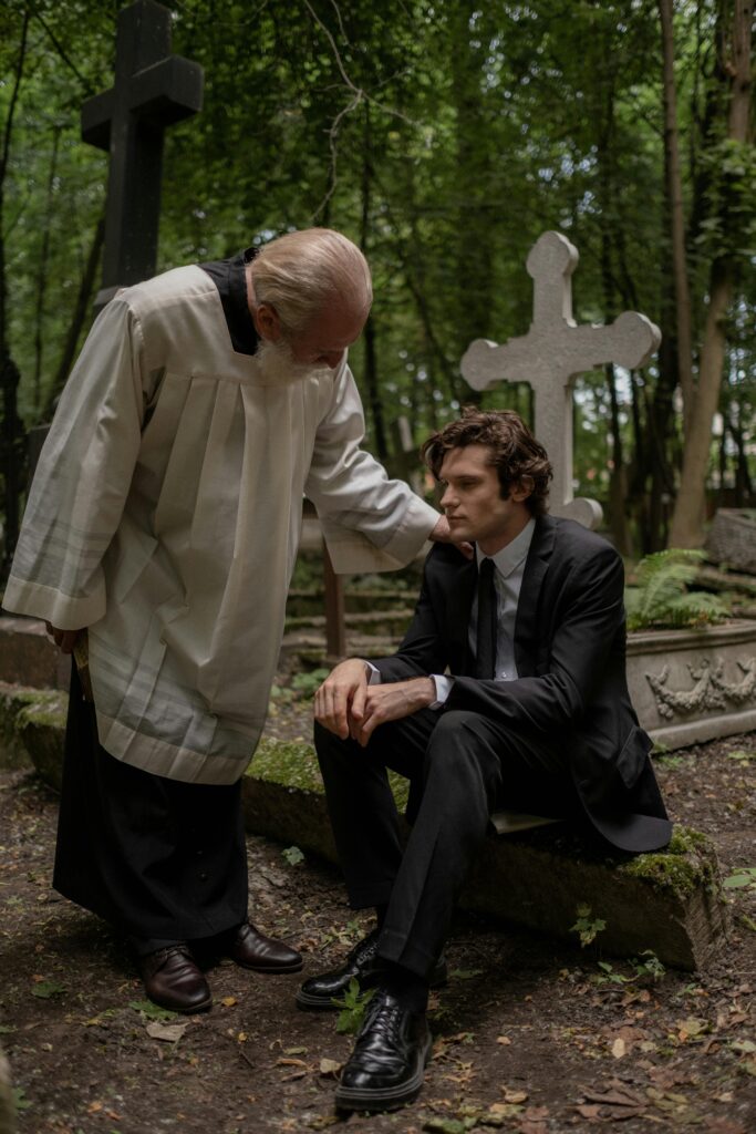 A priest consoles a grieving man at a cemetery, symbolizing support and compassion.
