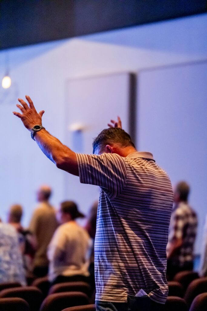 A man raises his arms during a vibrant church service, expressing worship.